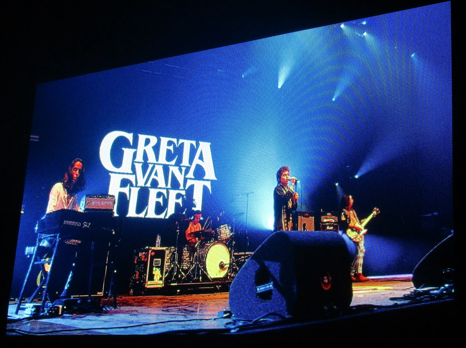 The full band on stage under the logo